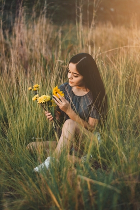 坐在野草丛中手持花枝的美女图片